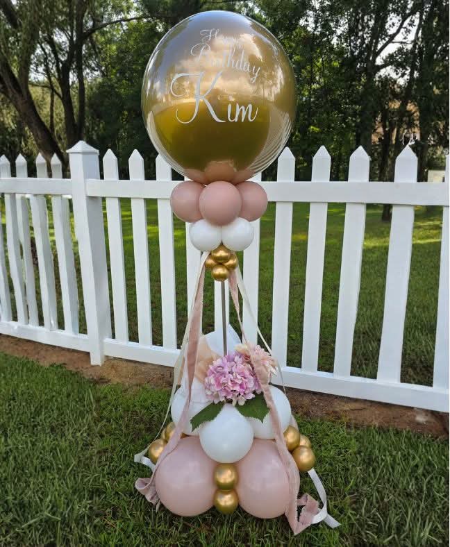 Personalized gold bubble balloon over a blush, white and gold floral column